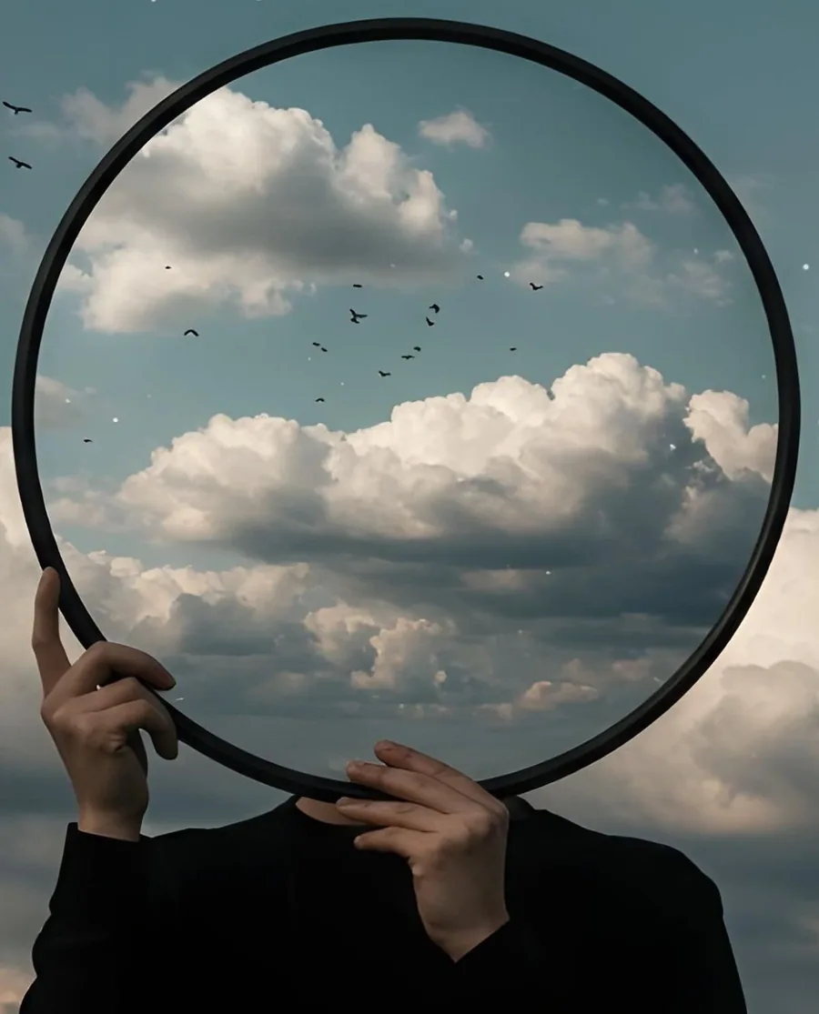 A hand holding a mirror that shows the sky behind the camera