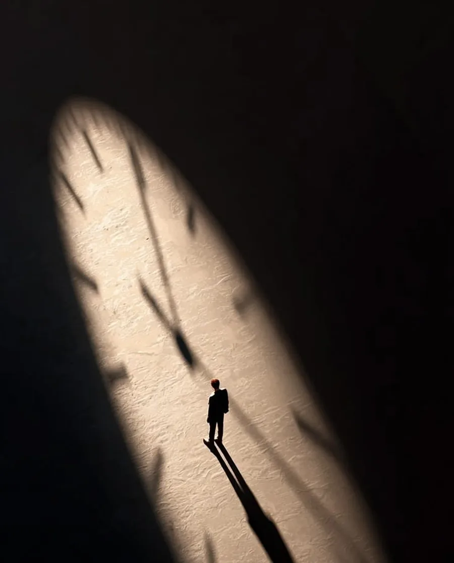 A single figure crossing a wall of light and shadow