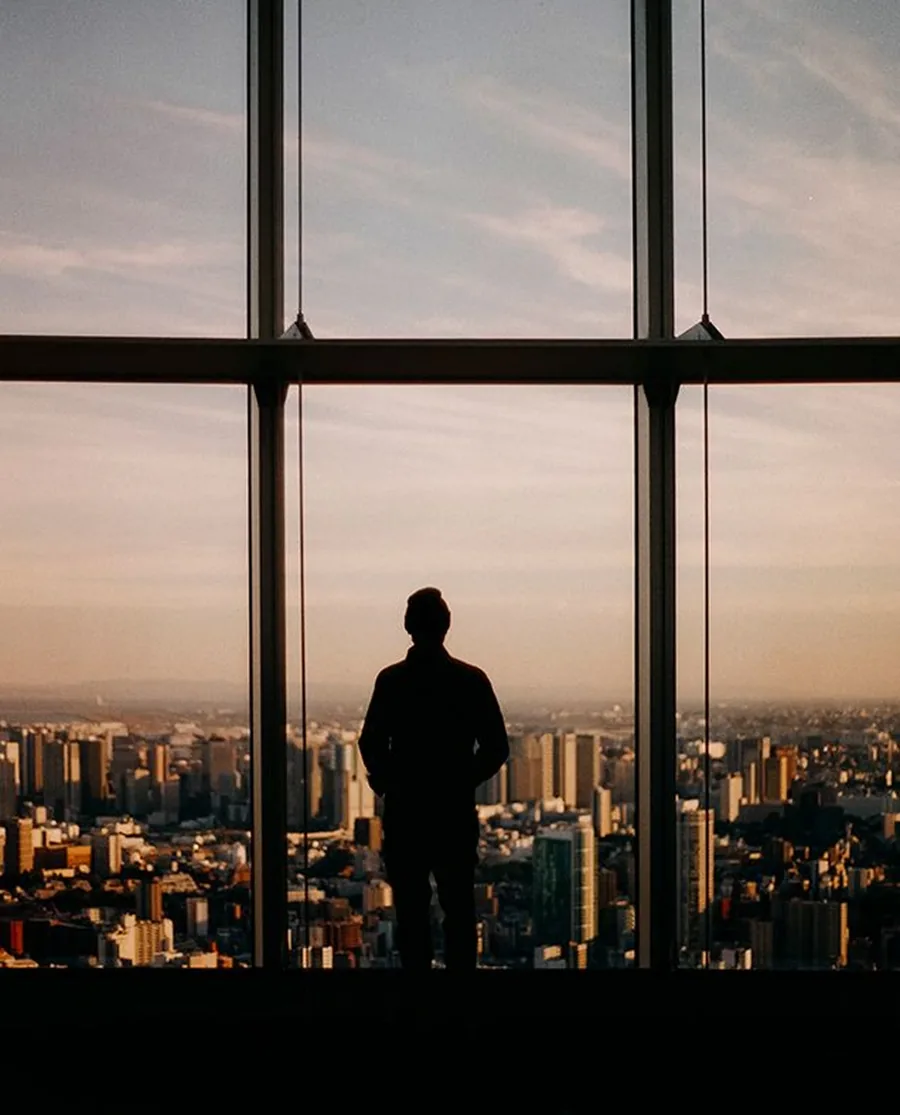 A figure at a window above a city at dusk