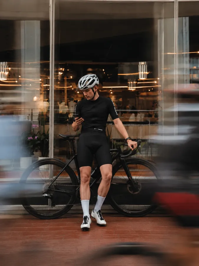 Mit dem Rennrad vor einem beleuchteten Schaufenster, Blick aufs Handy